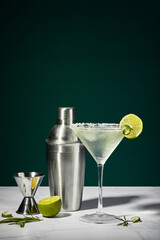 Martini cocktail with ice and slice of lime and shaker on a marble table. An alcoholic cocktail or...