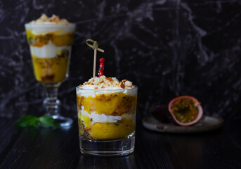 Mango and passion fruit trifle with cream cheese and home made biscuit and piece of passion fruit. Dark background, side view