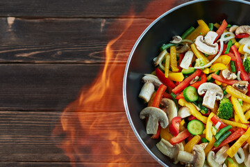 Wok pan with vegetables on wooden background, top view. Vegetables wok - peppers, onions, peas, mushrooms, beans, broccoli, zucchini. Asian food. Chinese food. Copy space