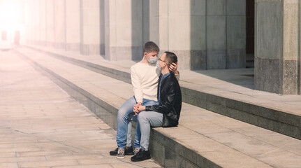 Young gay couple wearing medical mask hugging at city.