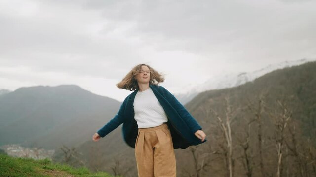 Young hipster woman in blue coat dancing in mountains 