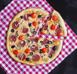 Homemade pizza with salami, mushrooms and cherry tomatoes on a black background. A red checkered towel. Top view.