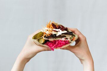 Closeup shot of hands holding vegetarian shawarma with red beans, and pickles wrapped in pita bread