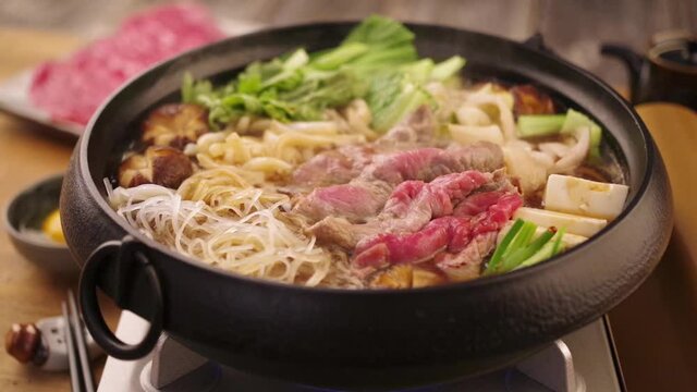 Traditional Japanese sukiyaki stew is boiling in a design cast iron pot