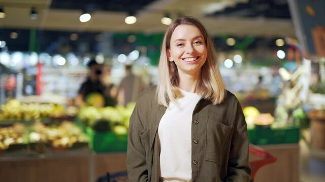 Portrait of a young active blonde woman. Female housewife in a grocery store, supermarket or market smiles happy and looking joyful at camera. Indoor shop Satisfied customer or buyer Vegetable section