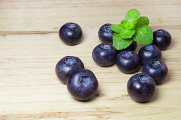 Ripe blueberries and mint leaves on a wooden background.