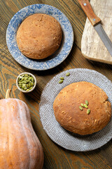 Two rolls of bread with pumpkin seeds are lying on ceramic plates, next to a pumpkin and a bread knife. Healthy food, top view, flat lay..
