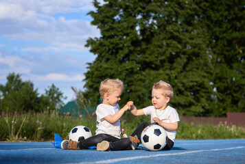 Twin brothers are playing on a walk.Two boys are sitting on the stadium surrounded by soccer...