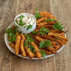 Baked pumpkin fries with tahini sauce on ceramic plate over wooden background.