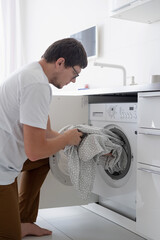 Young man putting clothes into washing machine