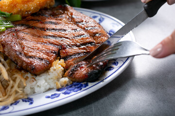 A view of hands cutting into a pork chop.