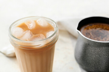 Glass of tasty iced coffee and pot on table, closeup
