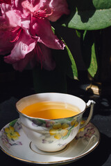 yellow floral teacup tea time with pink flower dark background in sun