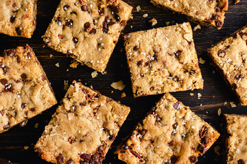 Brown Butter Bourbon Pecan Chocolate Chunk Blondies Garnished with Flaky Sea Salt: Blondies cut into squares and served on a dark wood cutting board