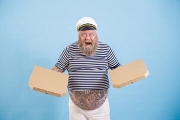 Excited mature man with overweight in sailor costume holds blank cardboard boxes of pizza standing...