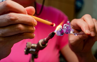 Hands of the glassmaker, making figurines from glass. Shaping hot Murano glass into a bunny under a jet of fire from a gas burner. Handmade fine art. Selective focus. Close up.