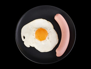 Fried egg and sausage on a black plate on a black background