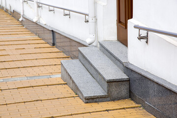 granite threshold at entrance door made of brown wood and white facade with plinth stone cladding of building and overflow storm pipe drainage system side view, nobody.
