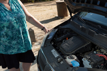woman looking at the engine on the road, heat wave, car breakdown, vehicle maintenance.