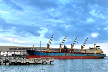 View from the water on the Bulk cargo ship under port crane bridge. Dry cargo terminal with cargo...
