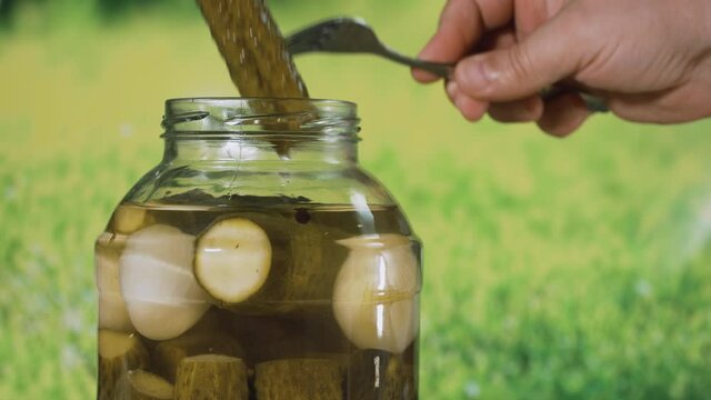 The man opens a jar of pickles and takes out two pieces in turn.  A jar of pickles on the table on a summer day outside the city. A man is preparing a snack for a party.