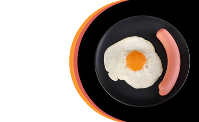 Fried egg and sausage on a black plate, on a black background, place under the text on a white background