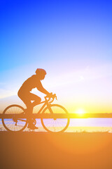 Fototapeta na wymiar Unrecognizable silhouette man riding bicycle against sunset sky. Road biking cyclist workout, riding racing bicycle on open road. Workout for triathlon. Dramatic sunset background, side view