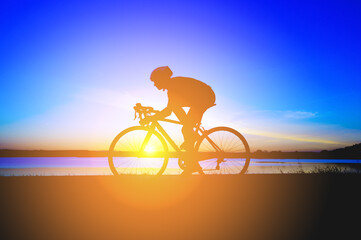 Unrecognizable silhouette man riding bicycle against sunset sky. Road biking cyclist workout, riding racing bicycle on open road. Workout for triathlon. Dramatic sunset background. side view