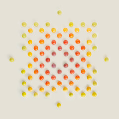 Geometric and symmetric shape made of green, yellow, orange and red wild plums isolated on pastel beige background. Natural, colorful summer fruit pattern. Minimal texture flat lay.