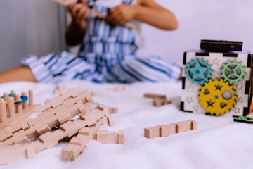 Fototapeta premium A boy with blonde hair in a jumpsuit plays children's educational wooden games in a bright room selective focus.