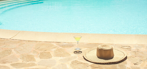Fototapeta na wymiar Minimal aesthetic summer vacation concept background with swimming pool. Straw hat and cocktail on a stone swimming pool side, clear blue water with waves. Fashion warm creative internet banner