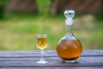 Homemade birch buds tincture in a glass bottle and a wine crystal glass on a wooden table