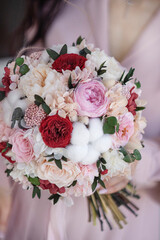 Classical bridal bouquet of preserved red rose and cotton flowers in hands. Bridal bouquet. Wedding bouquet of preserved flowers and cotton.