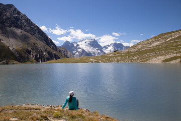 Fototapeta na wymiar Woman Sitting at the edge of Lac du Goléon in the French Alps with the Mountain Peak La Grave in the Distance