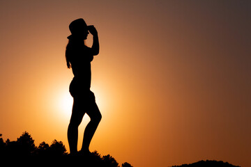 Silhouette of woman in profile at sunset, facing the sun, holding a hat in her hand. Selective focus. Copy space.