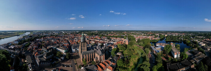 Super wide 180 degree cityscape aerial panorama of the Dutch medieval Hanseatic city with Walburgiskerk cathedral tower lit up in sunlight in urban landscape.