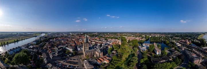 Foto op Plexiglas Super brede 180 graden stadsgezicht luchtfoto panorama van de Nederlandse middeleeuwse Hanzestad Zutphen in Nederland met de Walburgiskerk kathedraal toren verlicht in zonlicht in stedelijk landschap. © Maarten Zeehandelaar