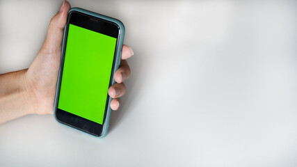 Man's hand holds mobile smartphone with green screen in vertical position, isolated on white background - mockup template and clipping path.