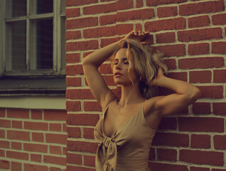 Sexy beautiful emotional blond woman posing in fashion gold color dress on brick wall background outside near the window. Closeup