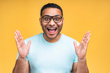 Surprised amazed african american indian man guy in casual isolated over yellow background studio portrait. People lifestyle concept. Mock up copy space. Keeping mouth open. - obrazy, fototapety, plakaty