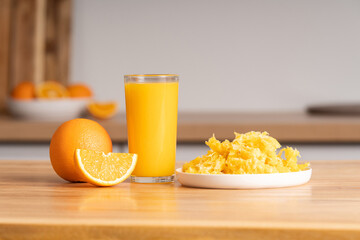 Glass of freshly squeezed orange juice on wooden tabletop, orange pulp in plate, close-up of orange slice.