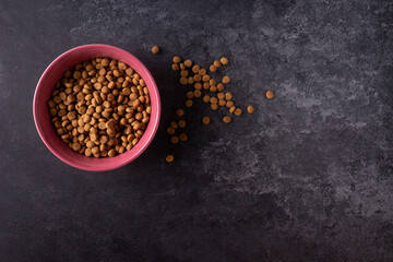 dry cat food in pink bowl on dark textured background