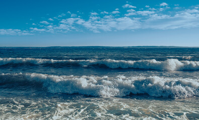 Rough white sea waves and white cumulus clouds in the blue sky