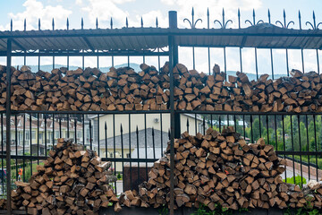 A stack of firewood by a metal fence under the roof.