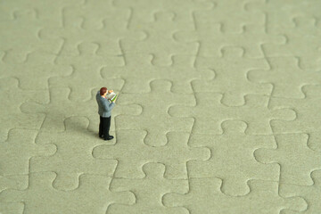 Miniature people toy figure photography. A men student standing above incomplete puzzle jigsaw