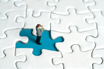 Miniature people toy figure photography. A men student standing above missing incomplete puzzle...