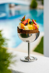 An exotic fruit cocktail in a chrome high-stemmed glass at a luxury resort with a blurred pool in the background. Foreshortening through vegetation