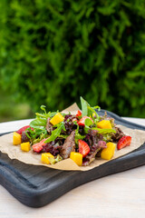 Salad with meat, strawberries, mango on a black wooden board. Luxurious resort overlooking the vegetation