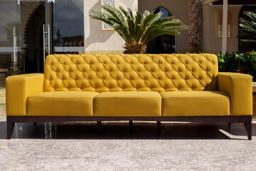 Bright yellow sofa stands in the outdoor patio on palm trees background