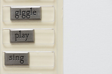 metallic tiles with the words "cry dance giggle play sing" still enclosed in their original package on a light background